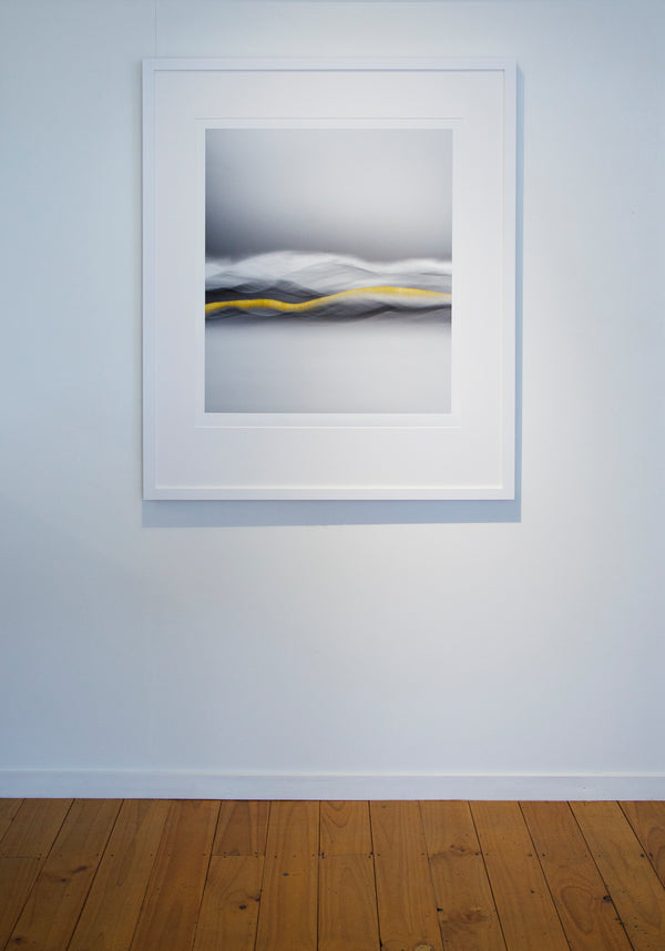 An in room image showing a framed limited edition print titled "vein of gold" print featuring abstract-style wave patterns with a central golden stripe, representing the history of gold in Central Otago set against a grey background.