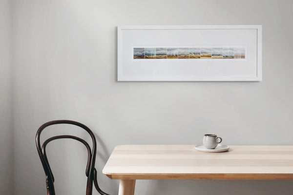 Framed artwork on a wall above a wooden table with a chair.