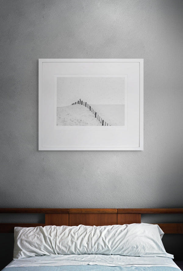 Framed artwork on a gray wall above a bed with white bedding.