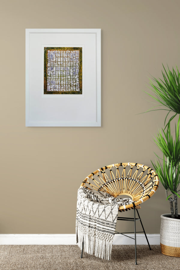 Wicker chair with a patterned throw blanket in a room with a framed artwork and a plant on a beige wall.