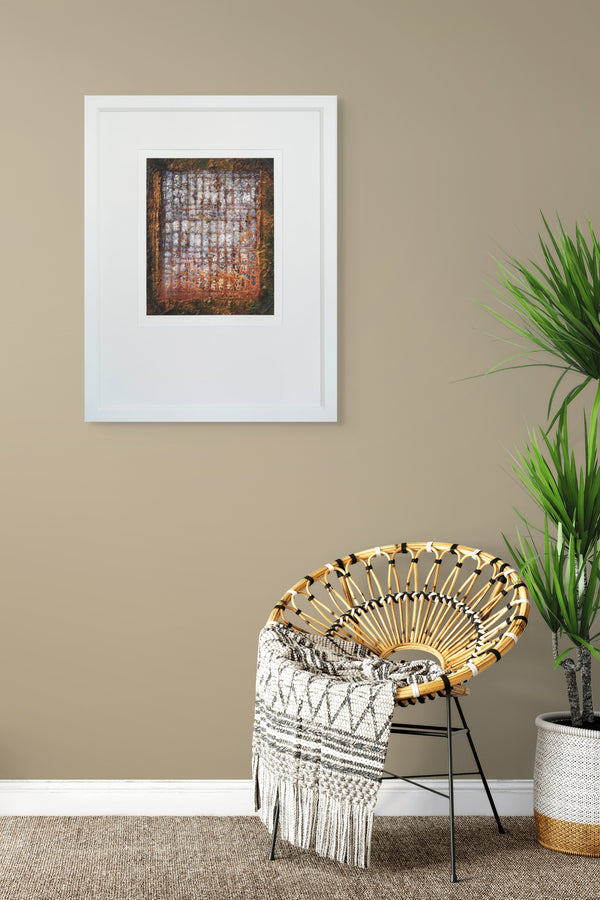 Woven chair with a patterned throw blanket against a beige wall with a framed picture.